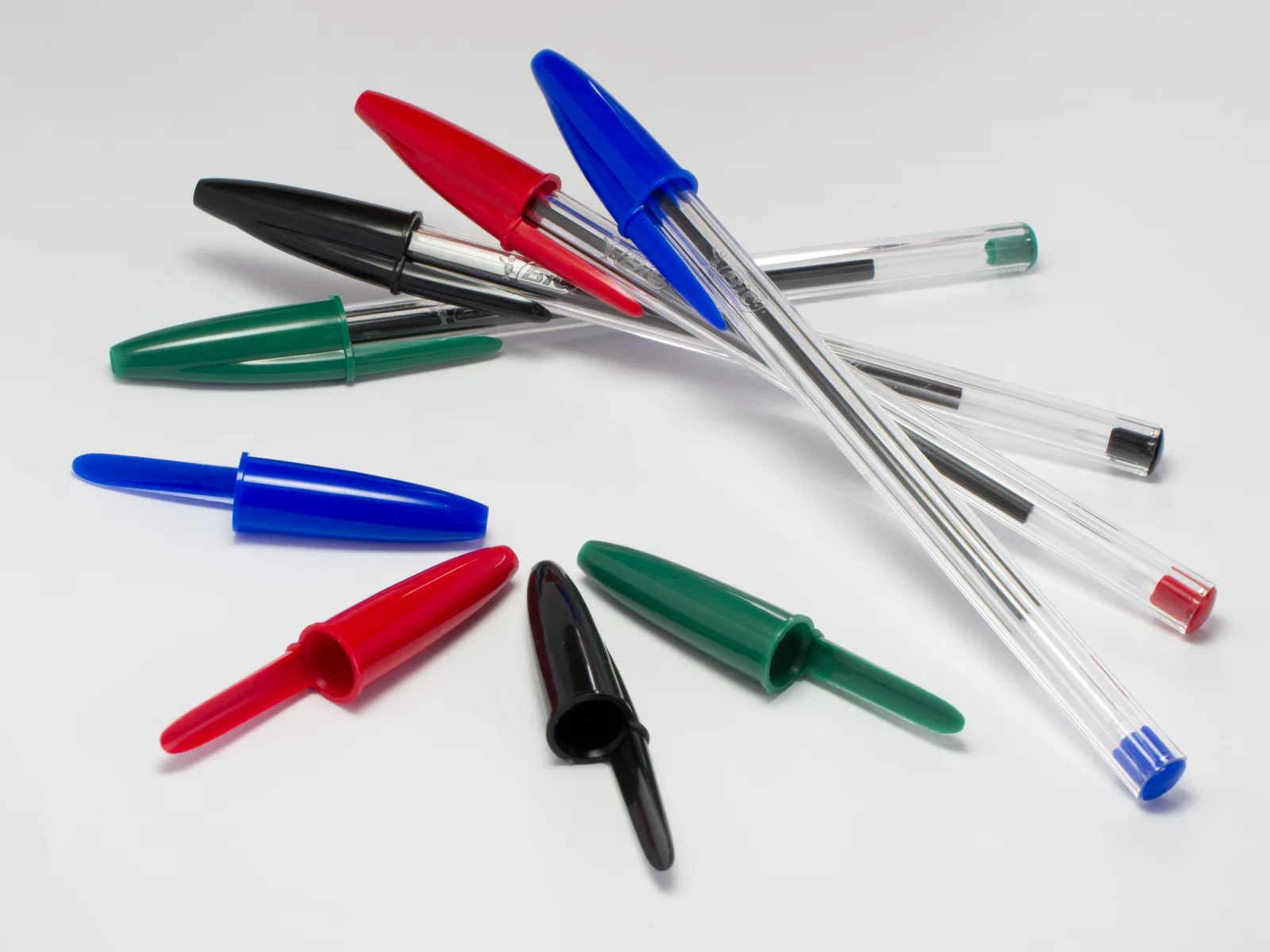 Des stylos Bic Cristal classiques (bleu, rouge, noir, vert) et leurs capuchons — le modèle standard dont dérive le « Bic Cristal for Her », dont aucune photo librement licenciée n’a été trouvée
